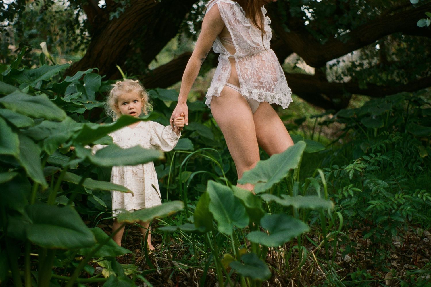 A playful moment captured in a lush garden setting with white fabric and greenery.