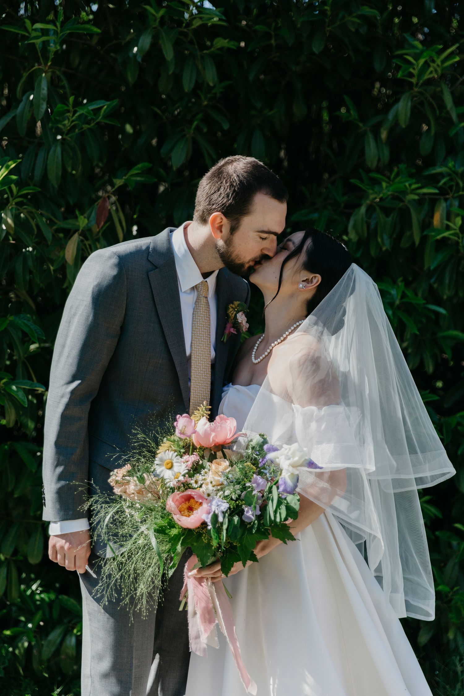 Romantic wedding couple sharing intimate moment with beautiful bouquet against green foliage.
