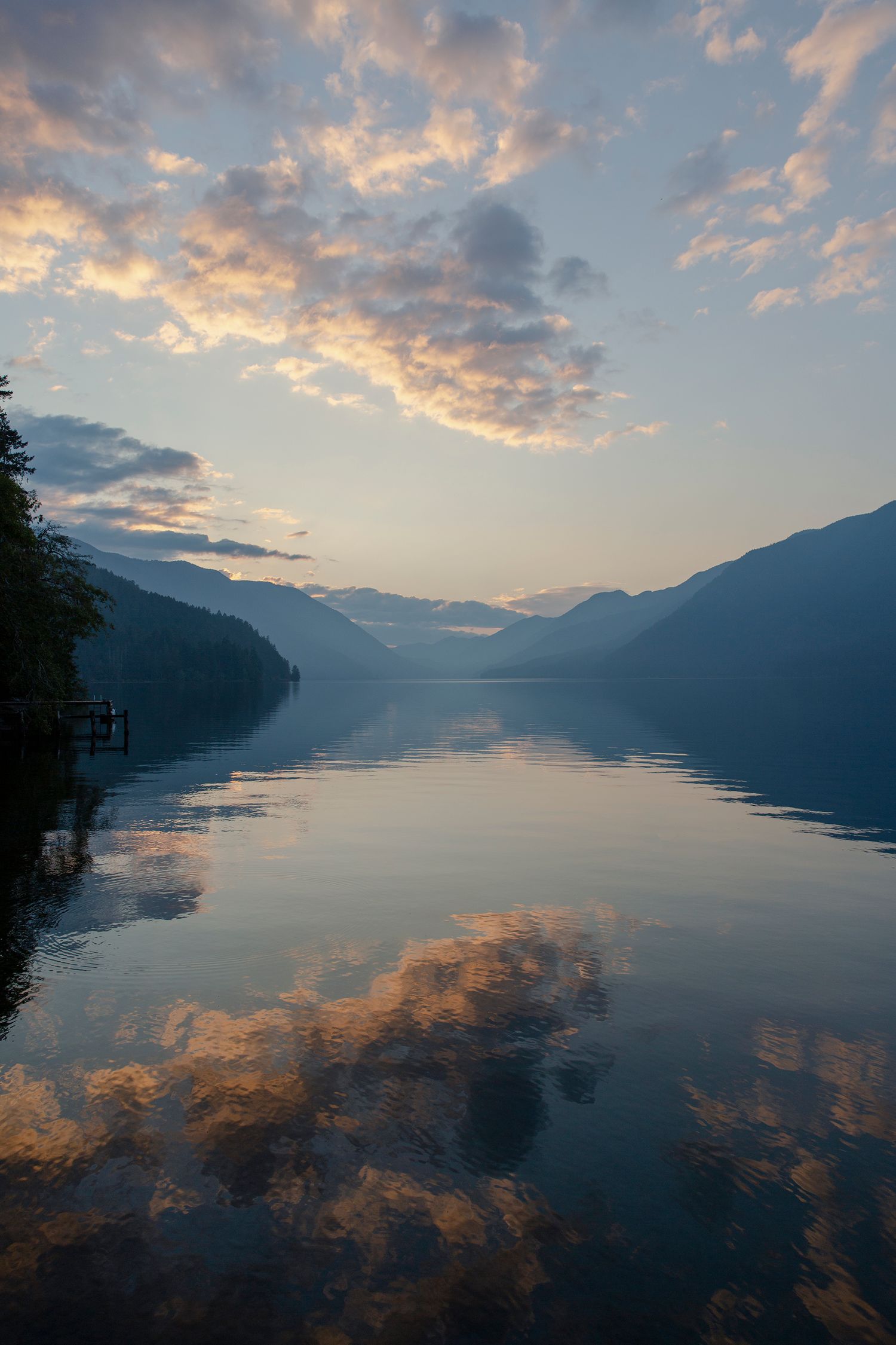 Sunset over a mountain lake with dramatic clouds reflecting in the still water.