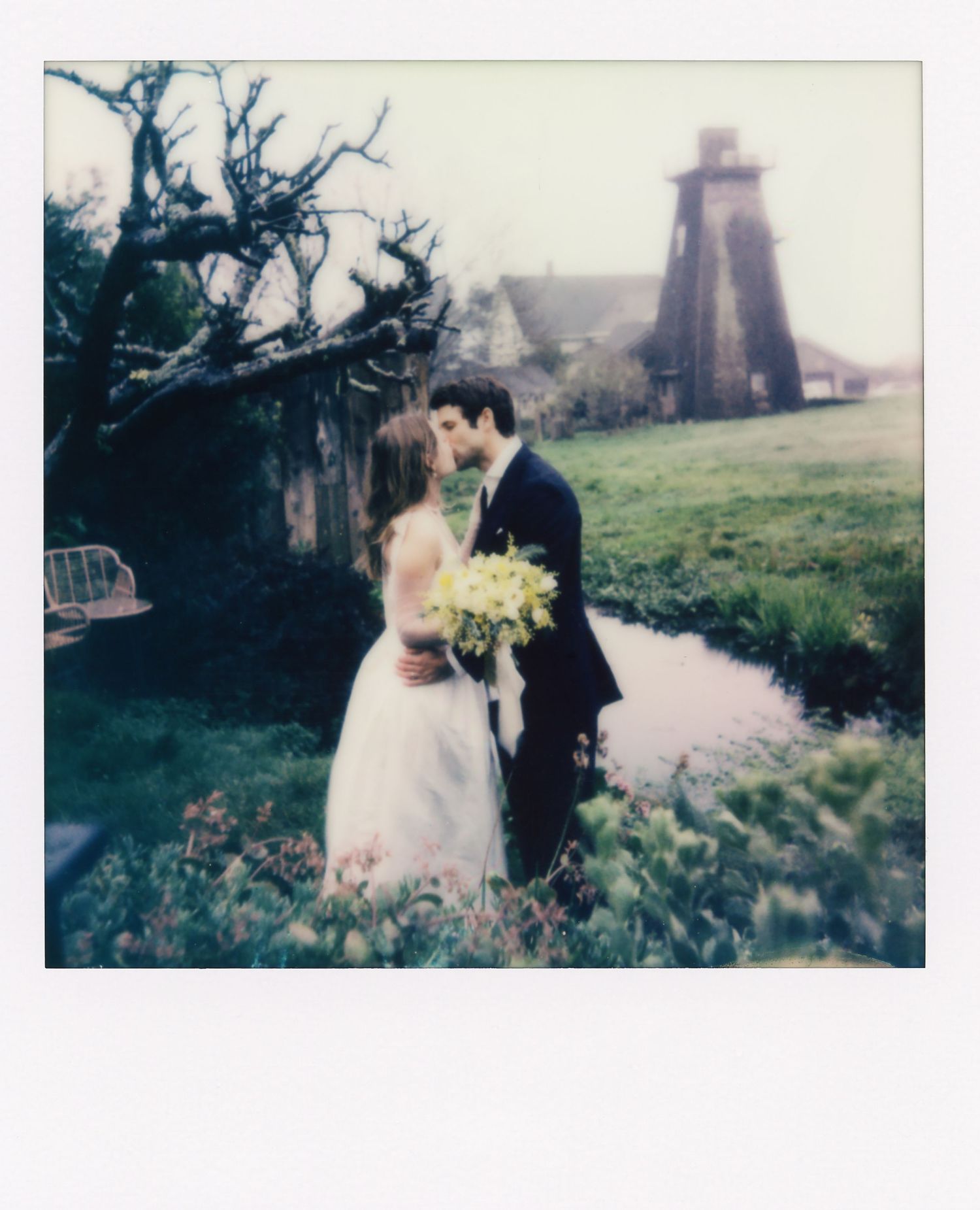 Dreamy polaroid wedding photo with couple near old lighthouse in muted tones.