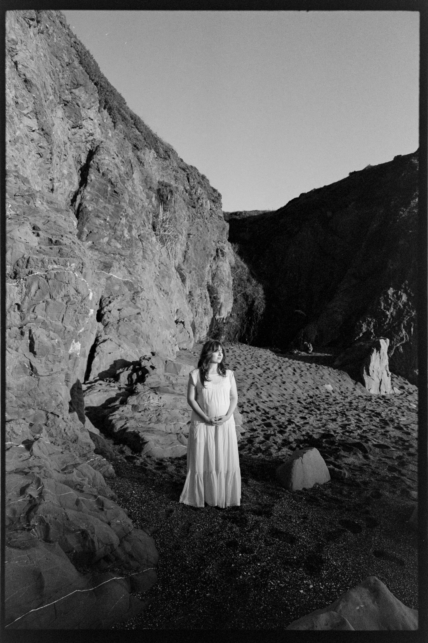 Black and white photo series showing figures in white dresses standing against dramatic rocky cliffs in a desert landscape.