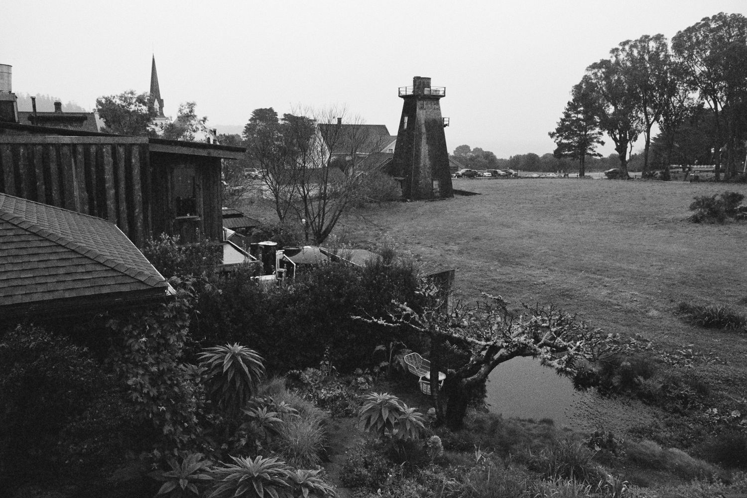 A black and white landscape featuring a wooden lighthouse structure and garden bridge.