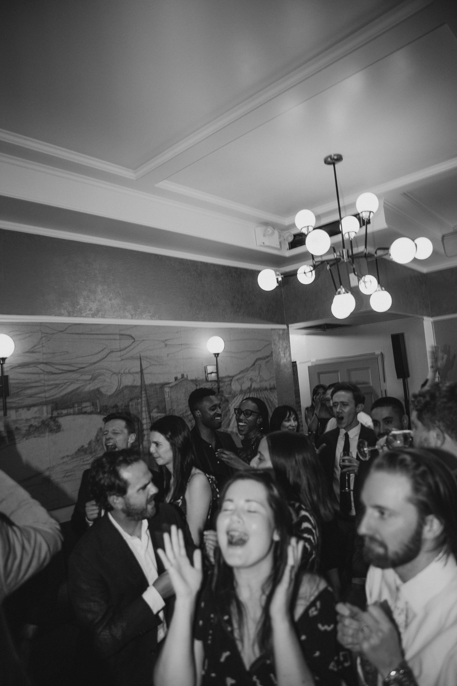 A lively indoor party scene with people dancing under a modern chandelier.