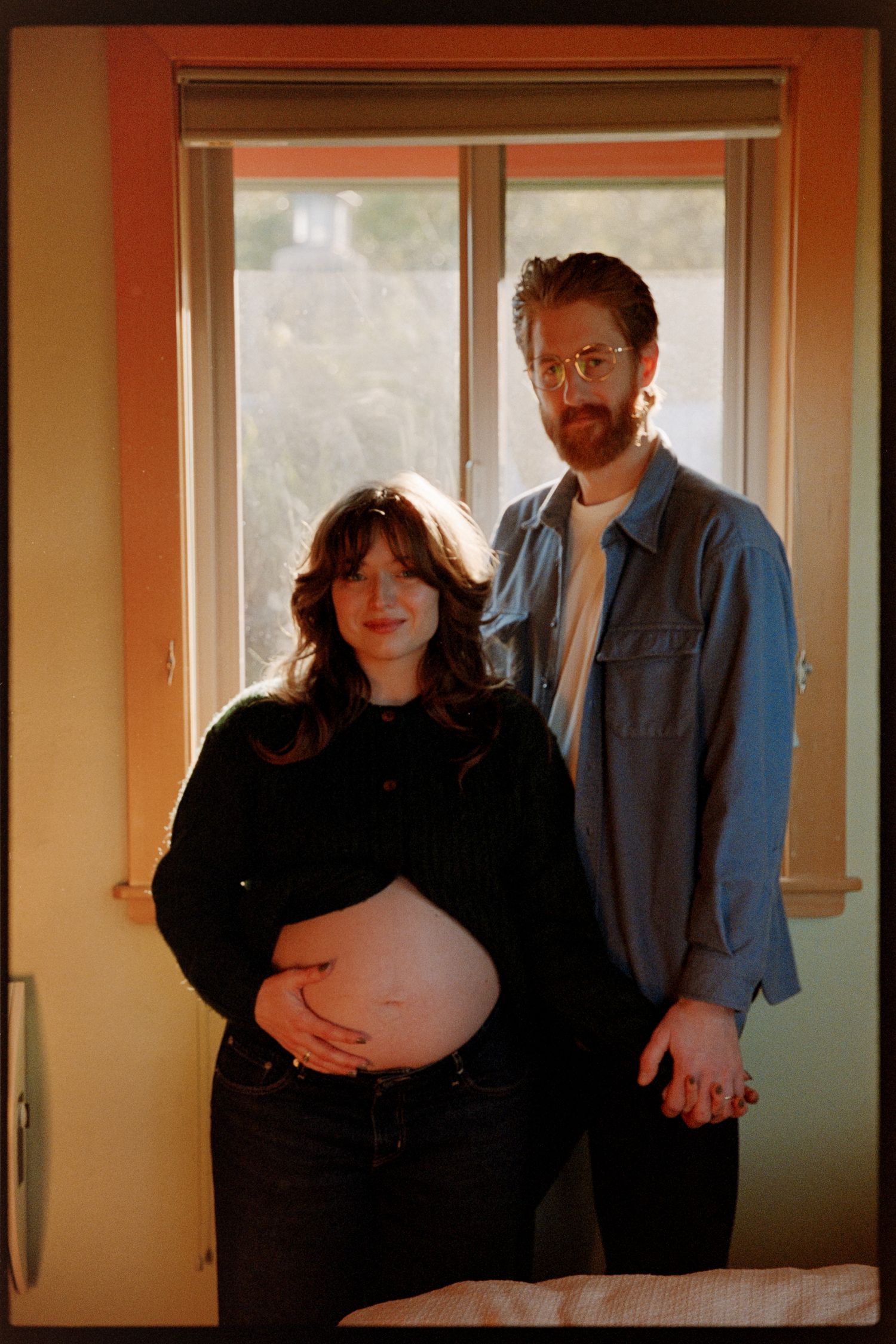 A series of four connected photos showing a couple during a maternity photoshoot in a warmly lit interior setting.