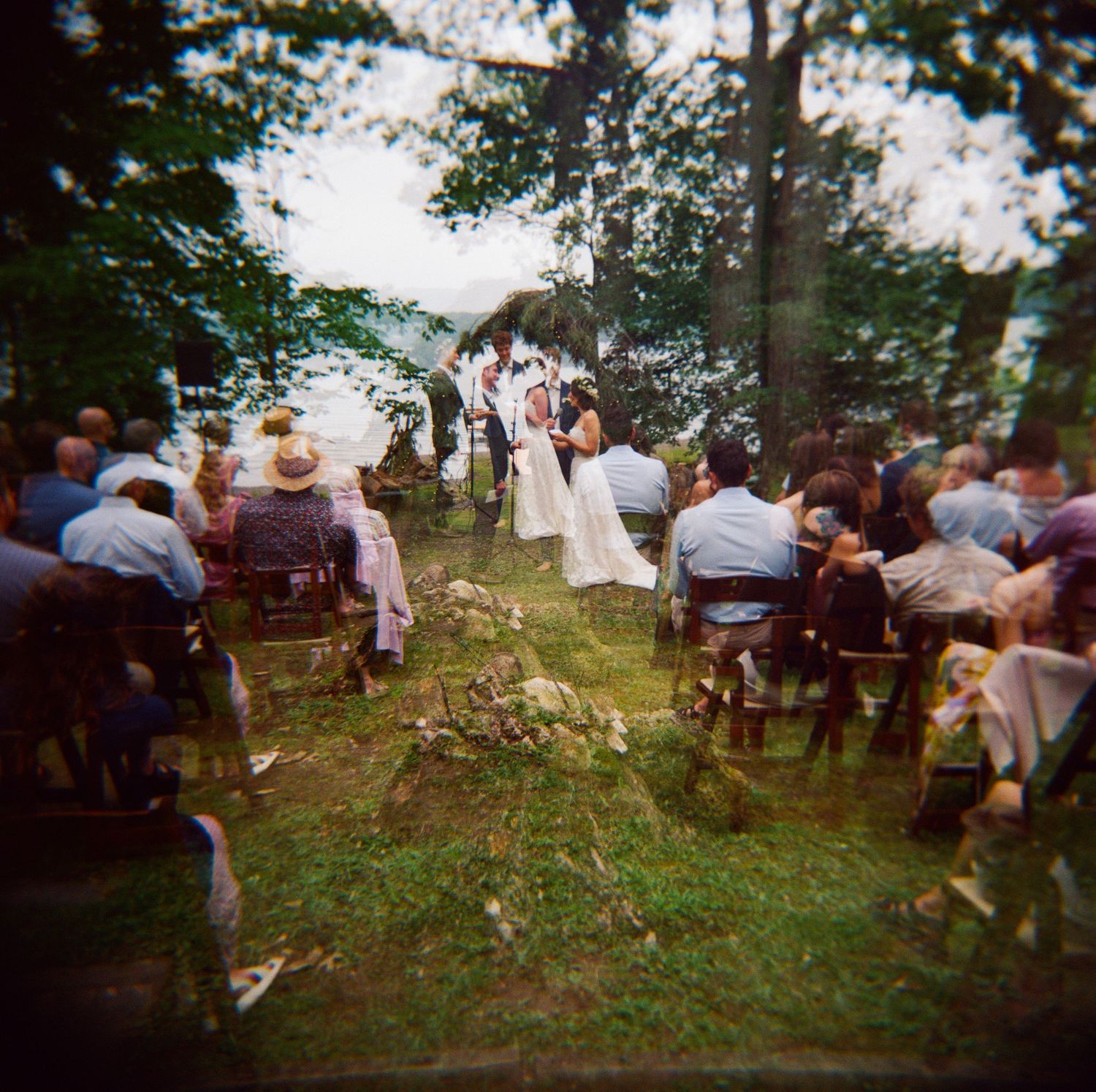 Outdoor forest wedding ceremony with guests seated on wooden chairs among the trees.