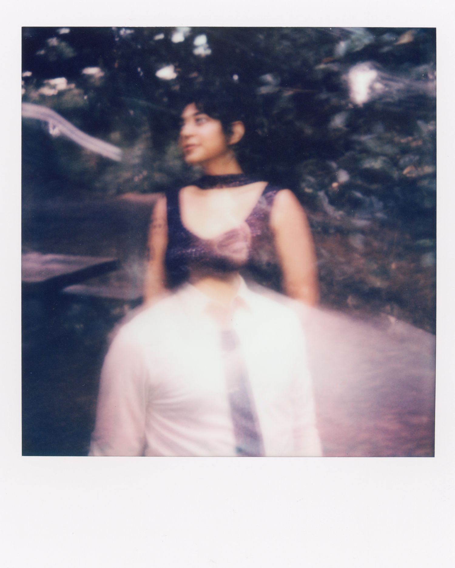 A vintage photograph showing someone in a white dress posing outdoors in a blurred, artistic composition.