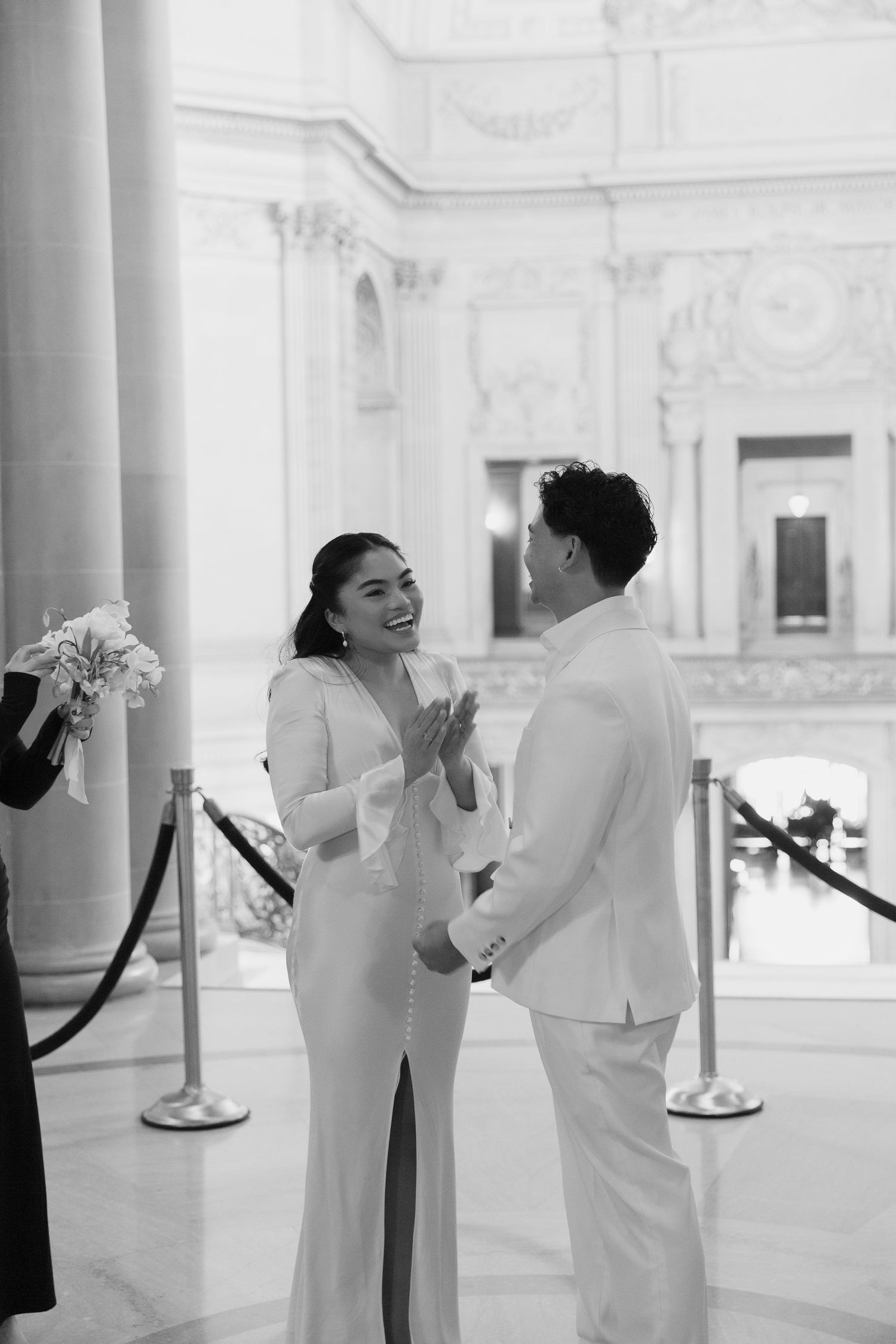 People in white outfits dancing joyfully in a bright, elegant room with classical architecture.