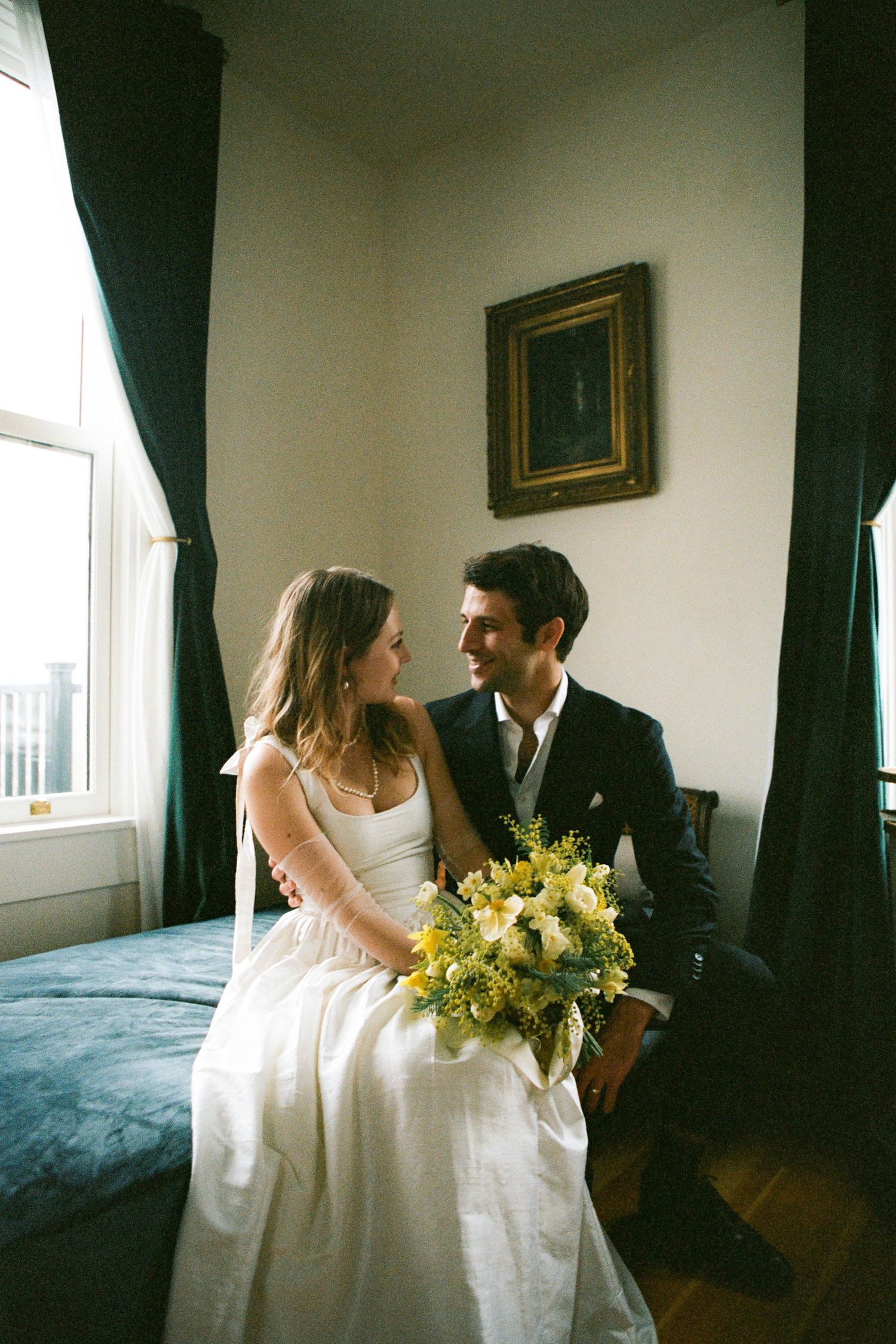 A couple shares an intimate moment in an elegant room with dark curtains and yellow bouquet in Mendocino.