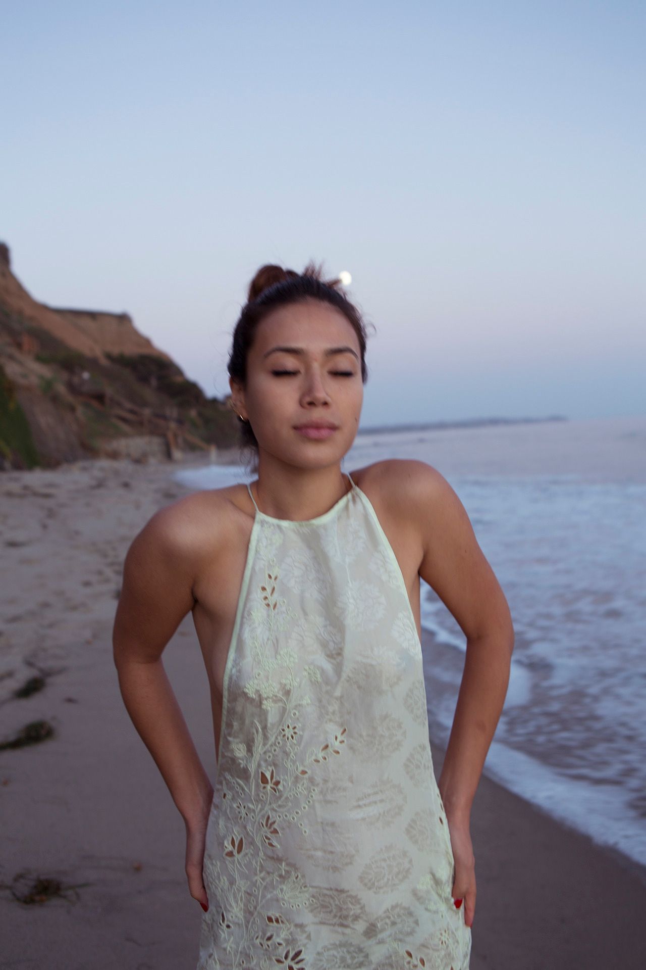 A romantic beach photo at sunset features a white halter dress against coastal cliffs and ocean waves.