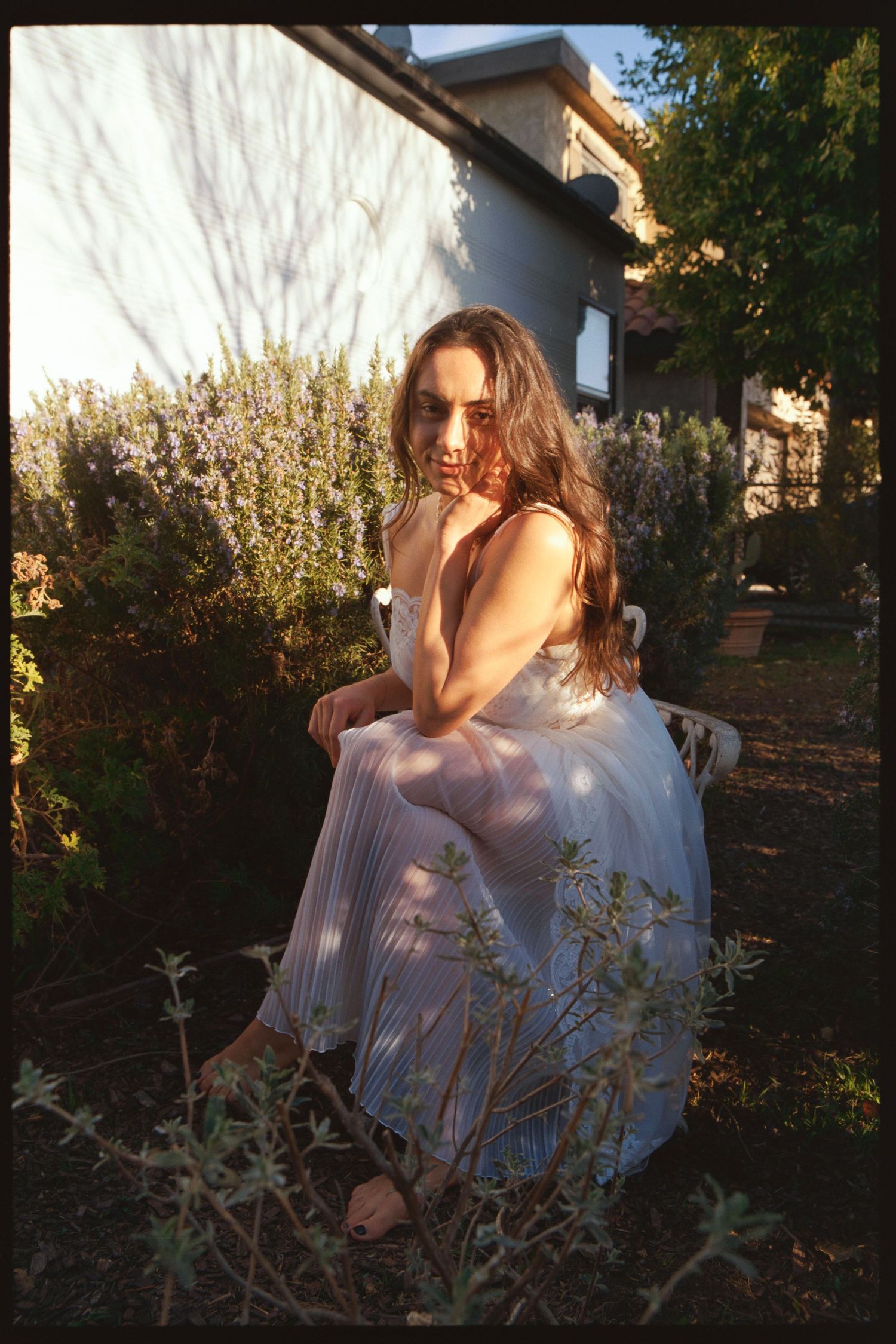 Woman in white dress sitting on garden bench surrounded by lavender and greenery in golden hour sunlight.