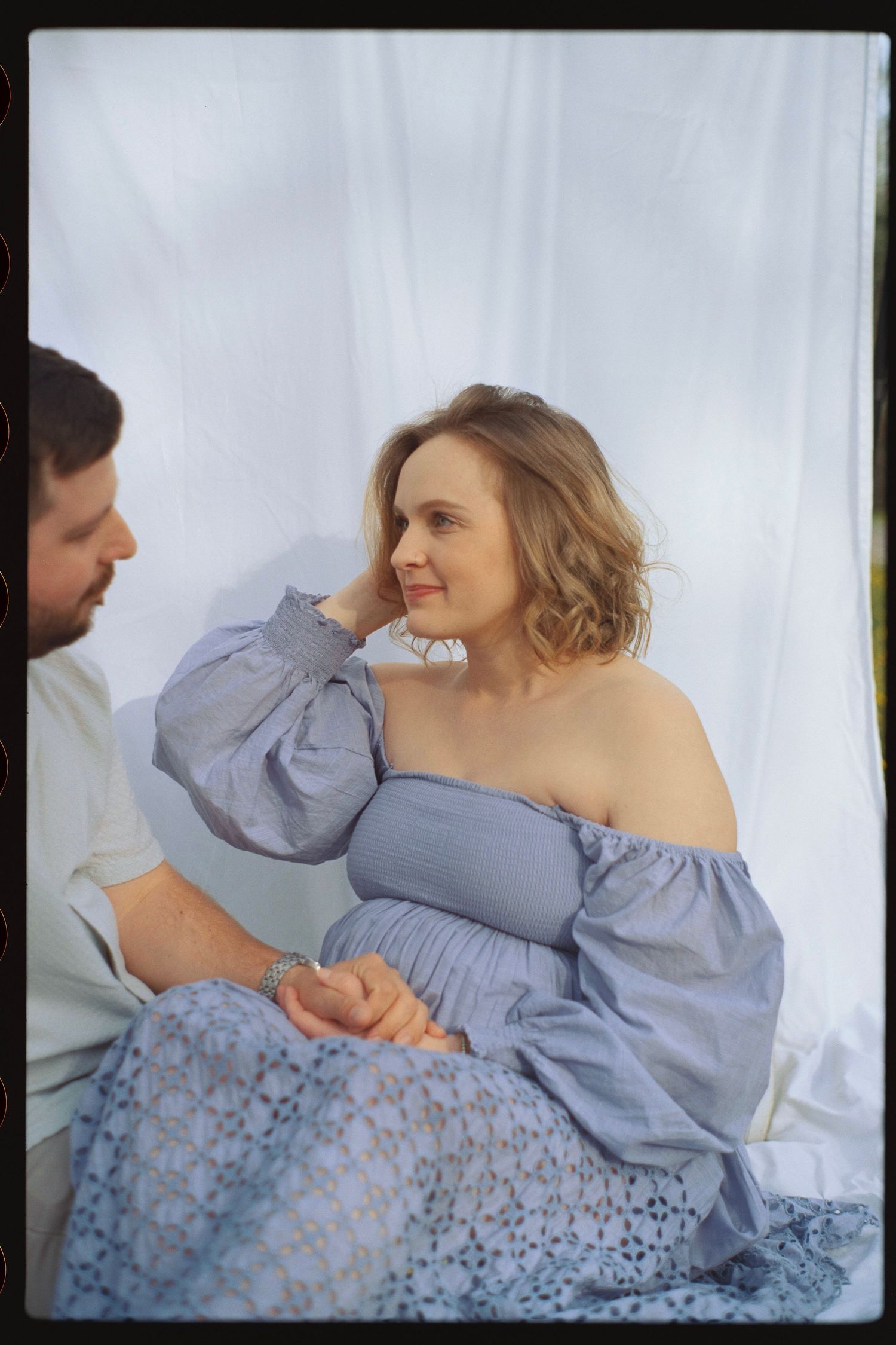 A tender moment captured between two people against a white backdrop, featuring blue lace dress details.