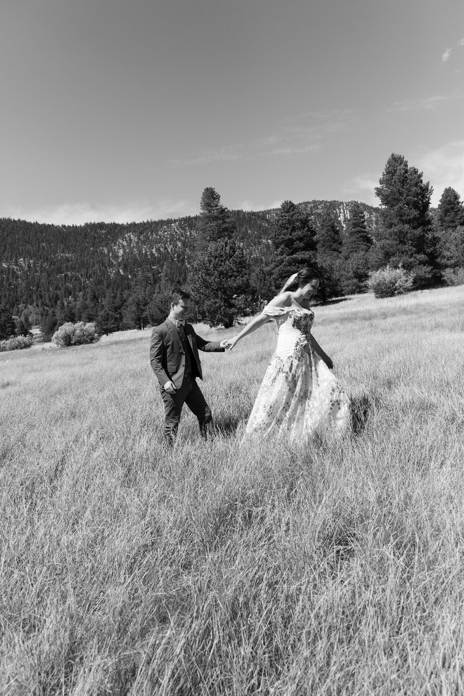 Wedding couple running playfully through tall grass in scenic mountain meadow in Tahoe.