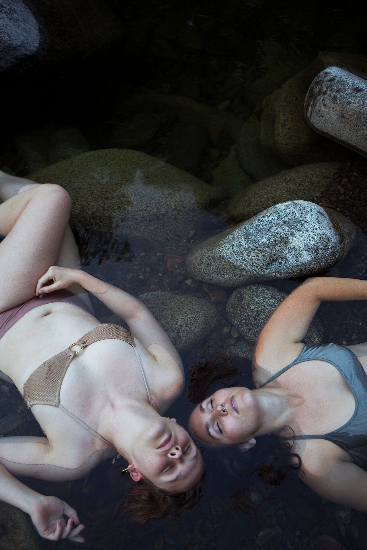 Models lying in shallow water with rocks in moody artistic composition.