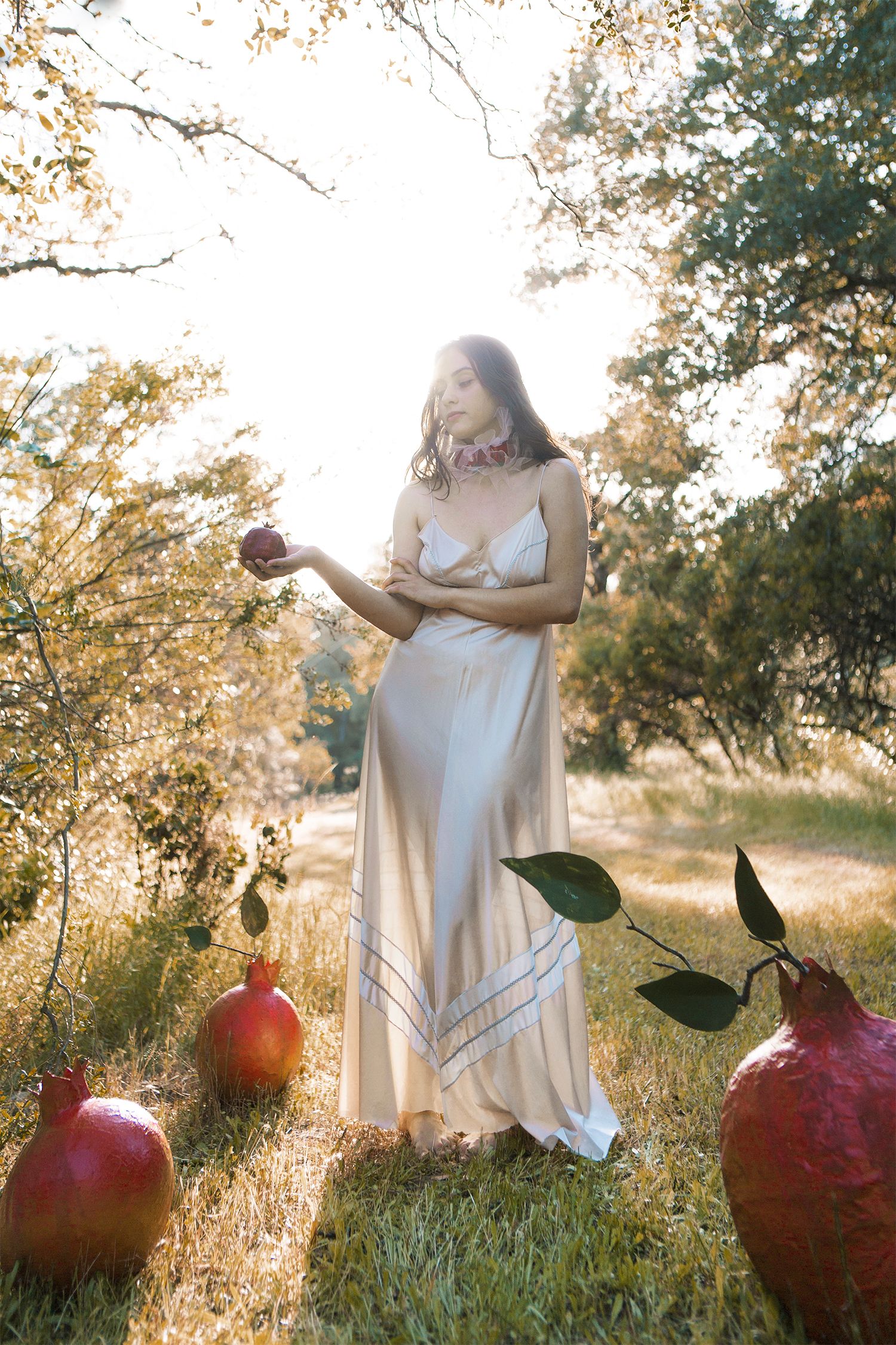 Dreamy garden scene with white dress and giant decorative pomegranates in golden sunlight.