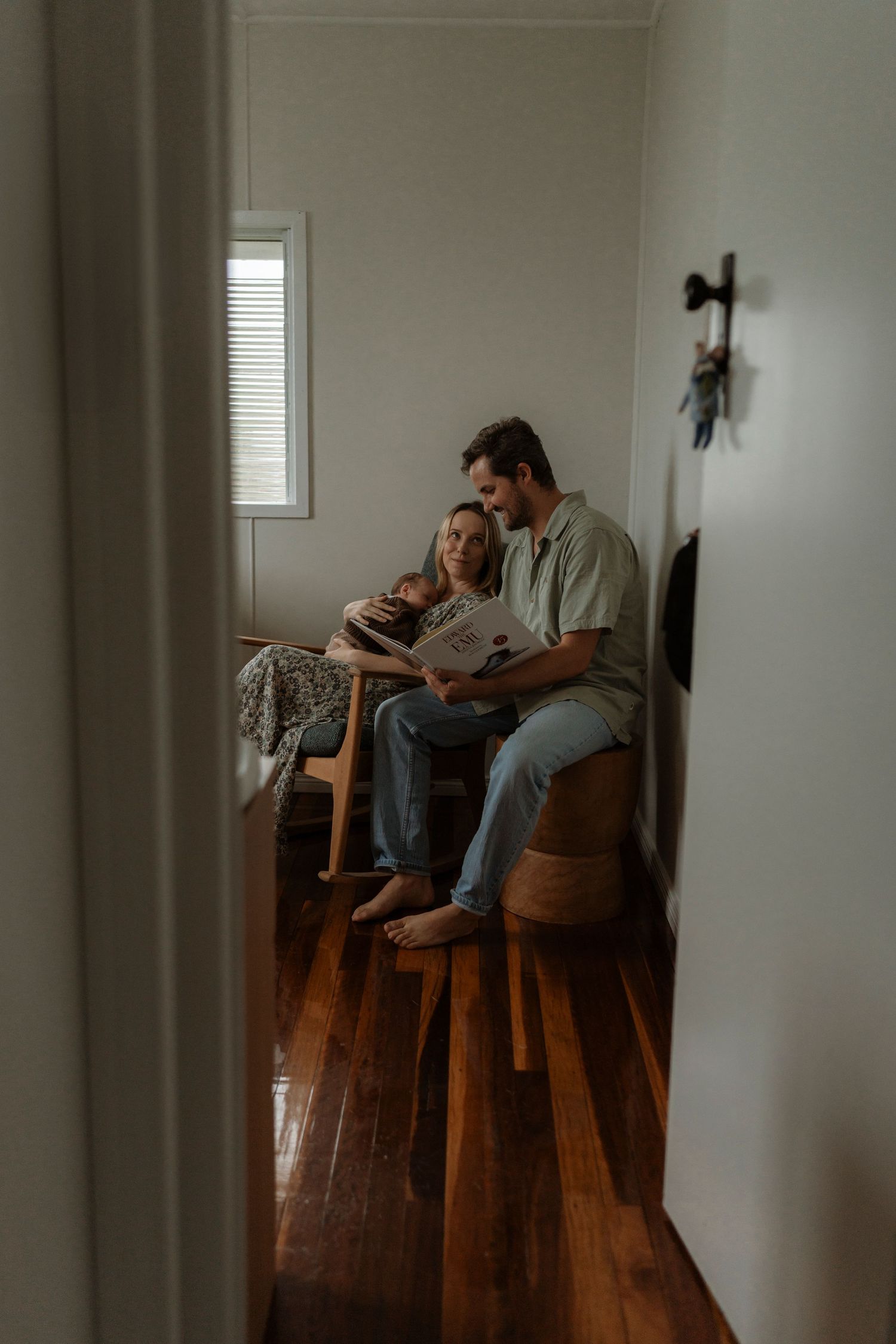 A couple sits together on wooden barstools in a minimalist room with hardwood floors and natural lighting.