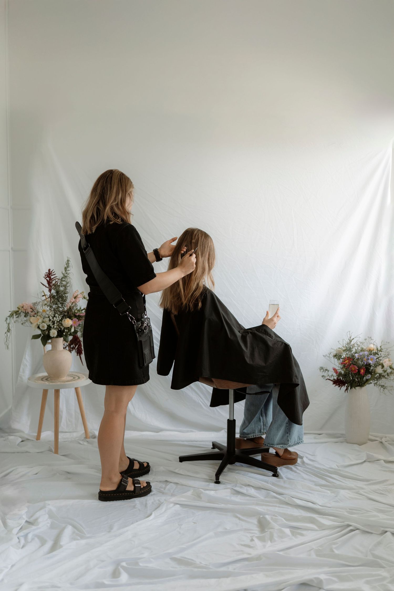 Behind the scenes styling shoot with floral arrangements and white backdrop showing salon chair setup in studio.