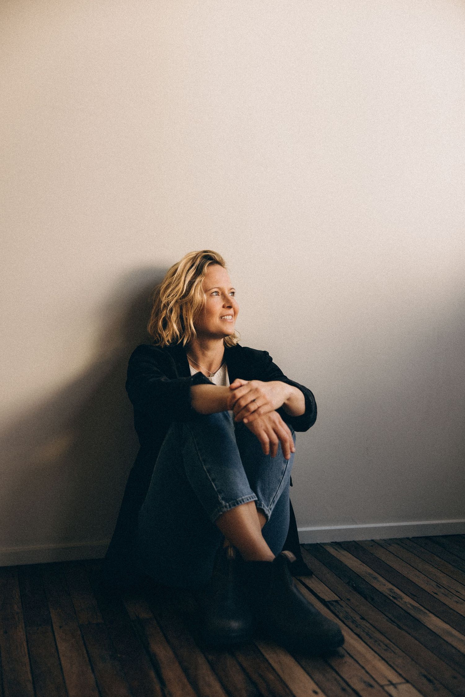 Person sitting alone on hardwood floor against white wall looking up in contemplative poses.