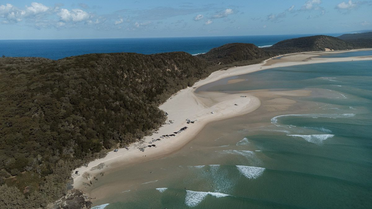 Aerial view of a stunning sandy beach cove surrounded by lush green hills meeting turquoise ocean waters.