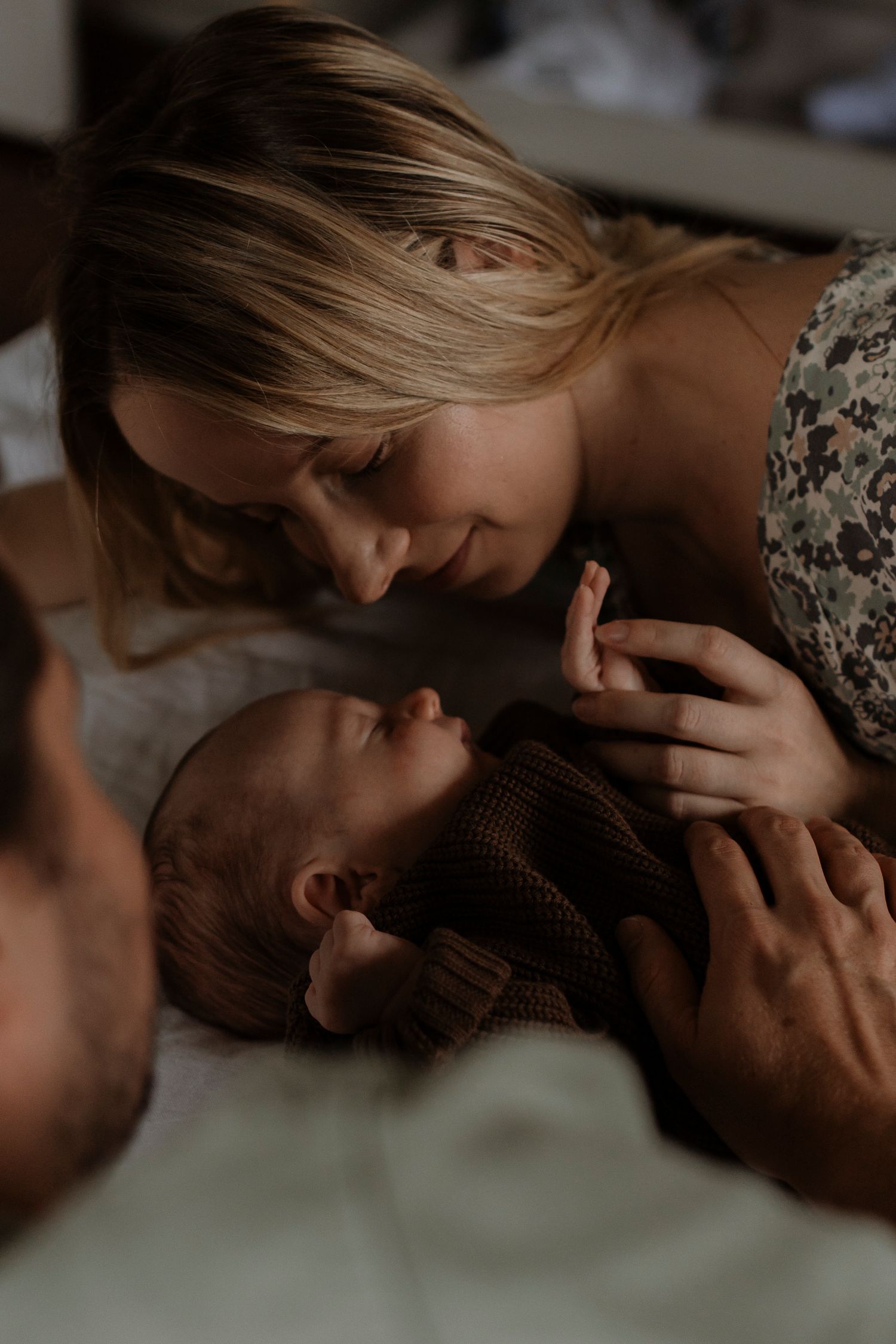 A mother tenderly gazes at her newborn baby while a father holds the infant on a soft white blanket.