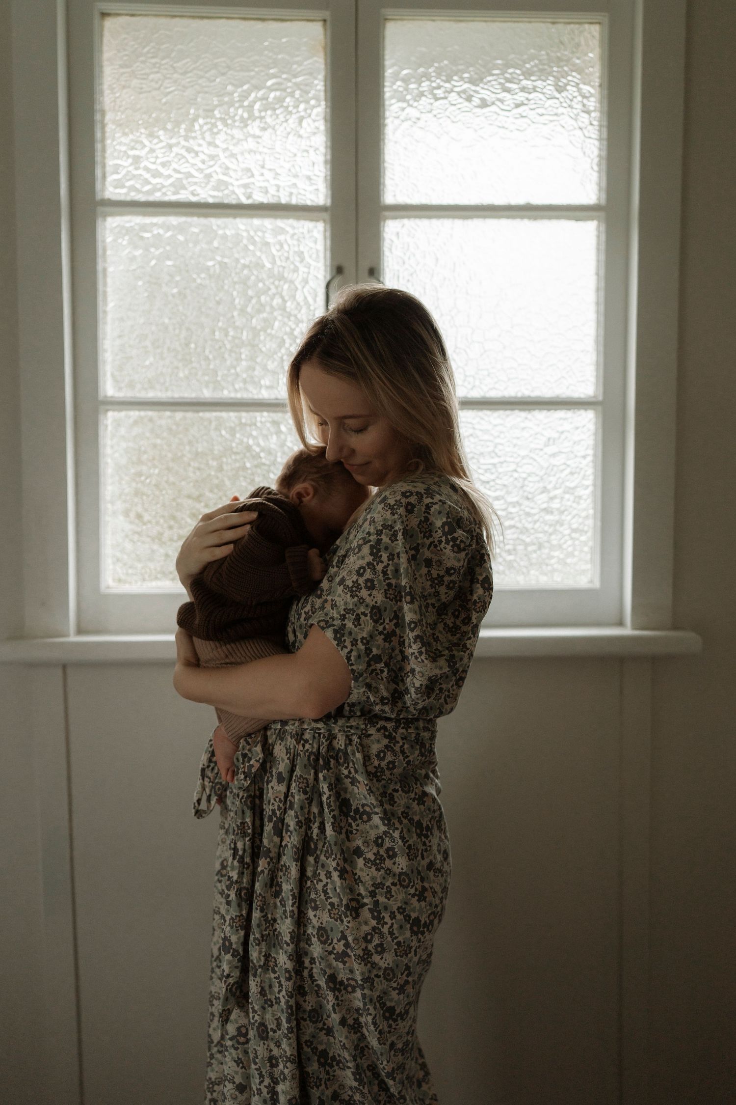 Two people embrace in a tender moment by frosted windows in a minimalist white room.
