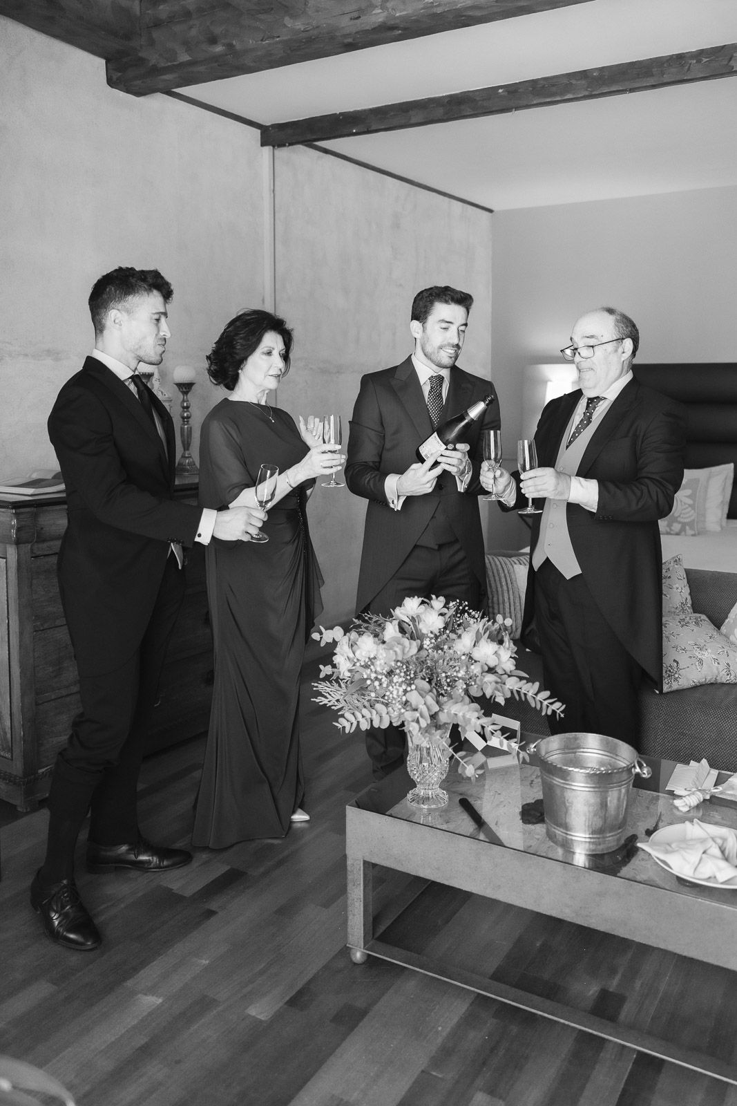 Black and white photo of elegantly dressed guests toasting with champagne at a formal celebration indoors.