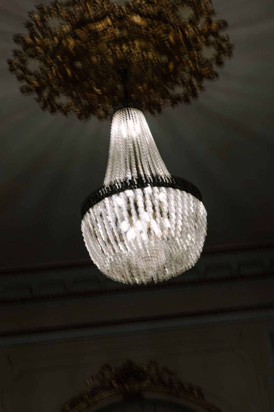 Elegant crystal chandelier with ornate golden ceiling medallion in a grand interior.