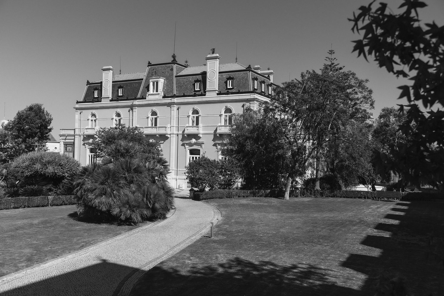 Black and white photo of a grand French-style mansion surrounded by lush trees and manicured lawns.