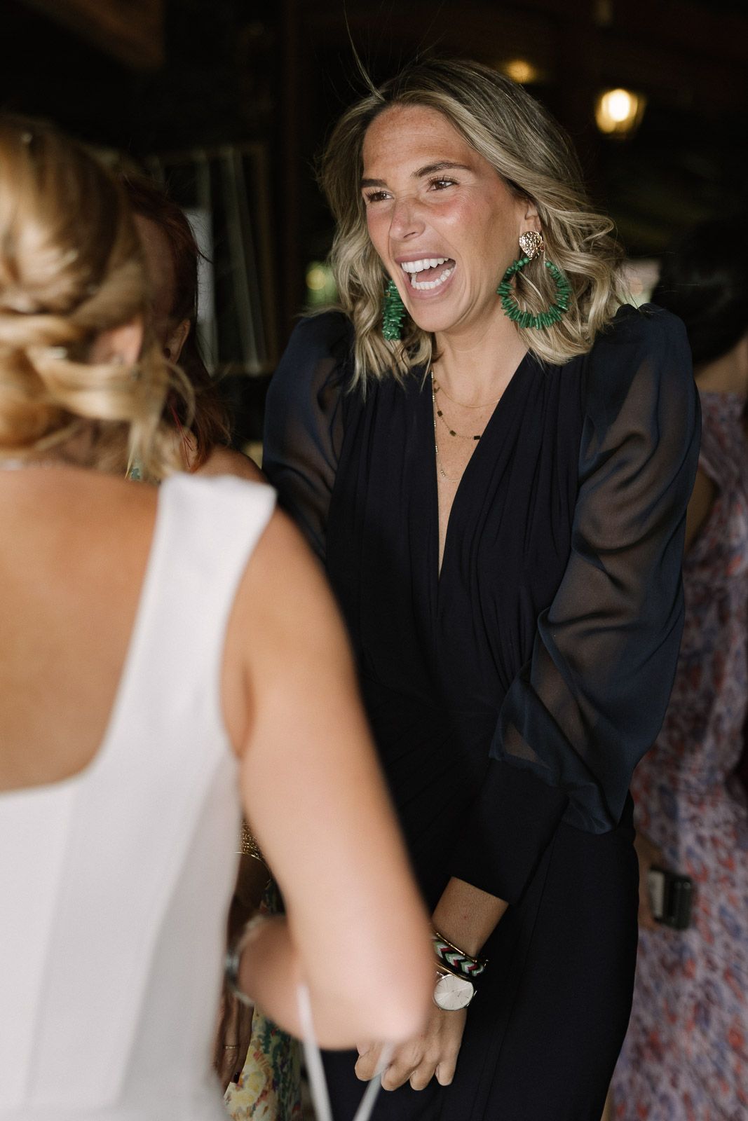 Woman in black dress laughing joyfully while talking to another guest at a social event.