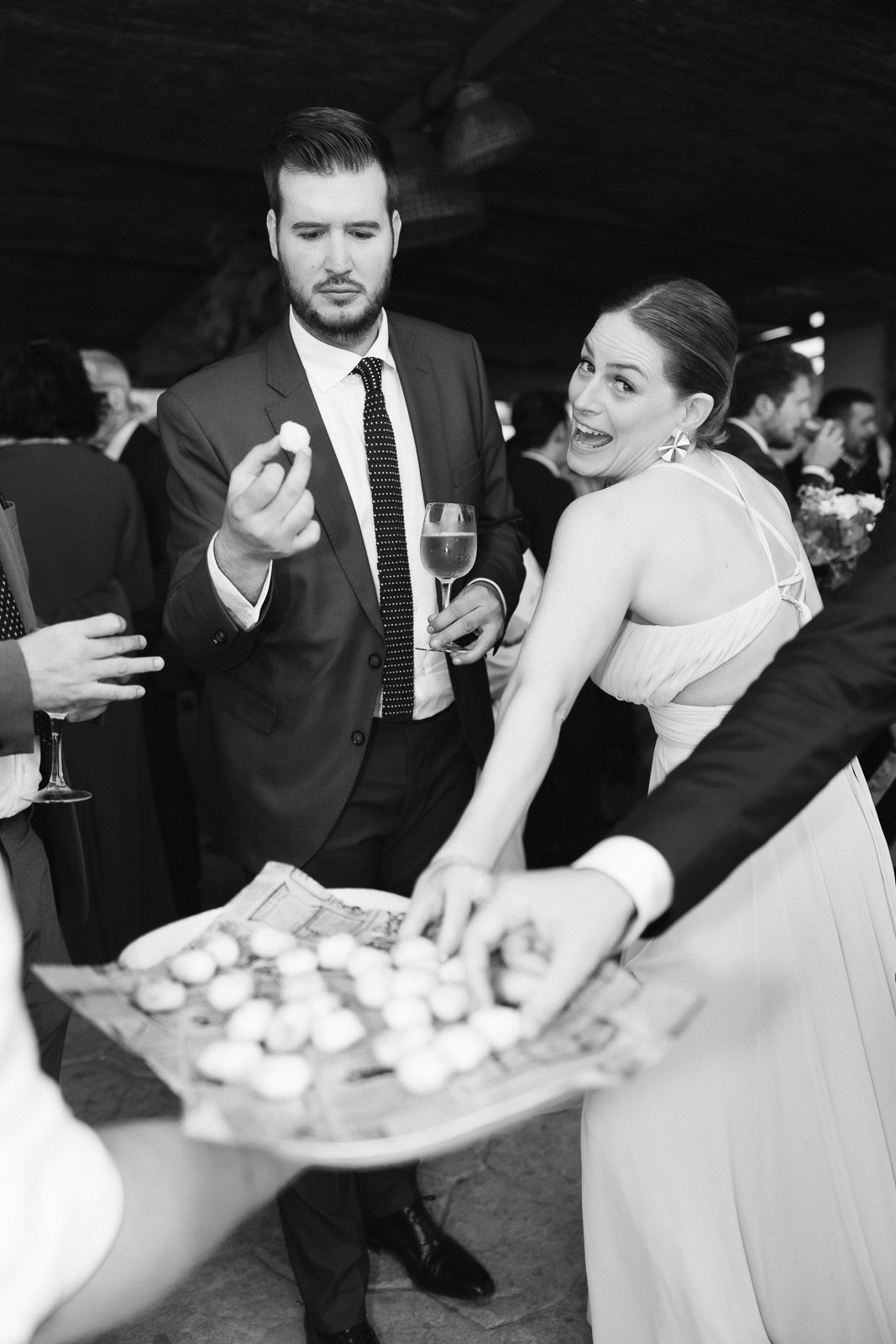 Black and white photo of elegantly dressed couple at formal event, woman reaching for hors d'oeuvres from a tray.