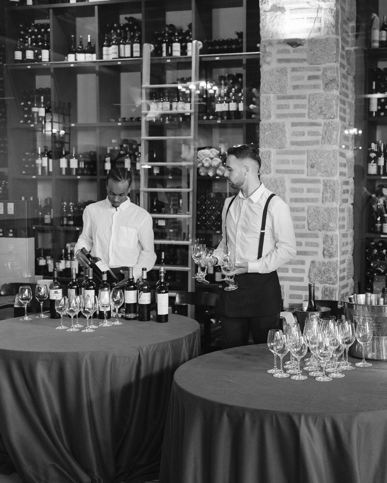 Two bartenders preparing wine glasses at an elegant wine bar in black and white.