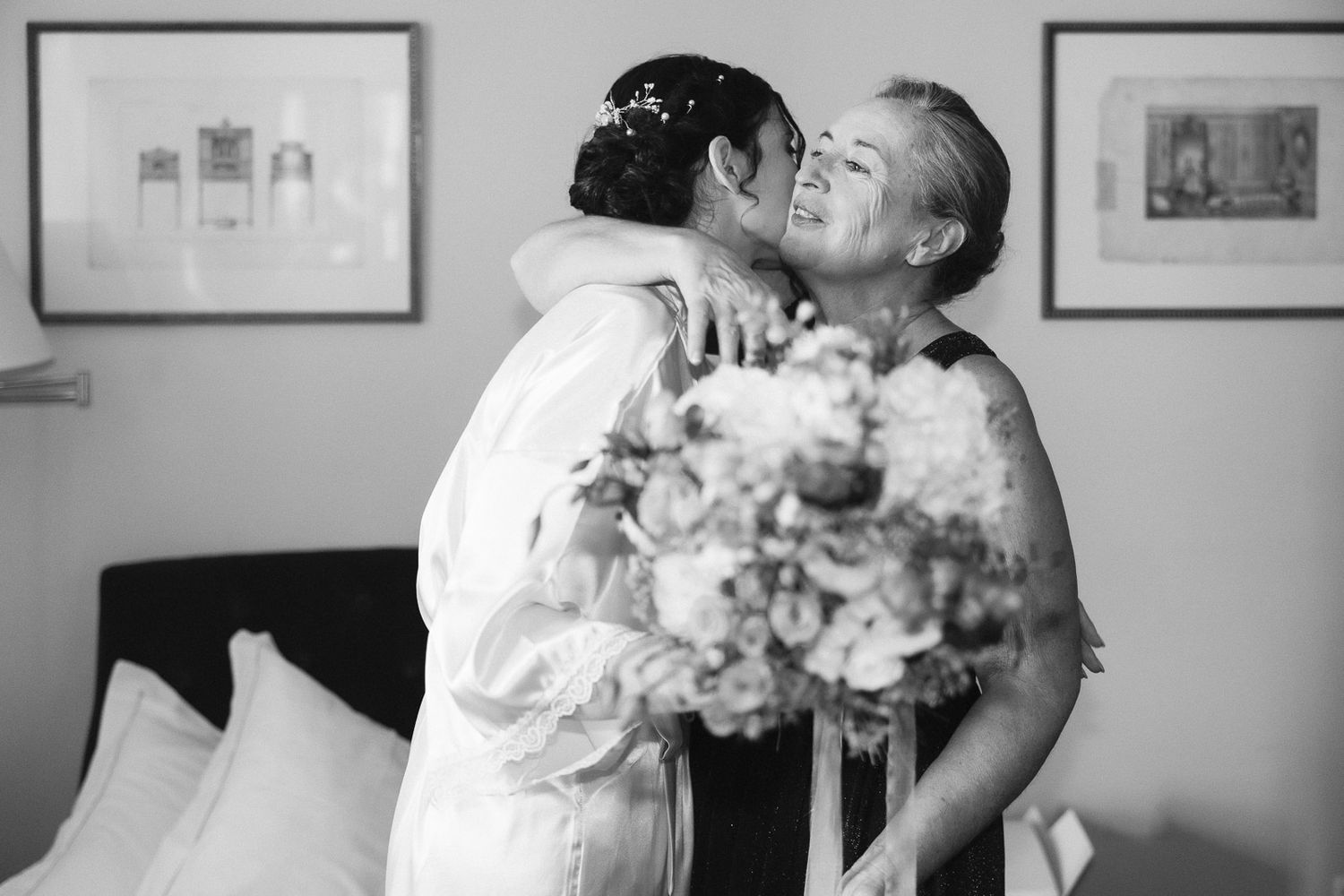 Black and white photo of a bride hugging an older woman while holding a bouquet, sharing a joyful moment.