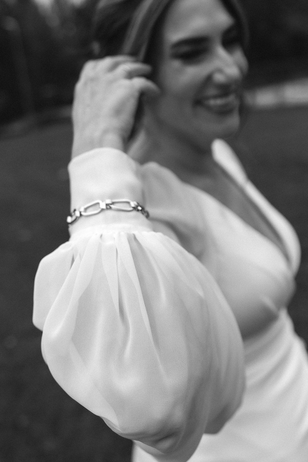Black and white photo of a smiling bride in a white gown with puff sleeves and a chain bracelet.