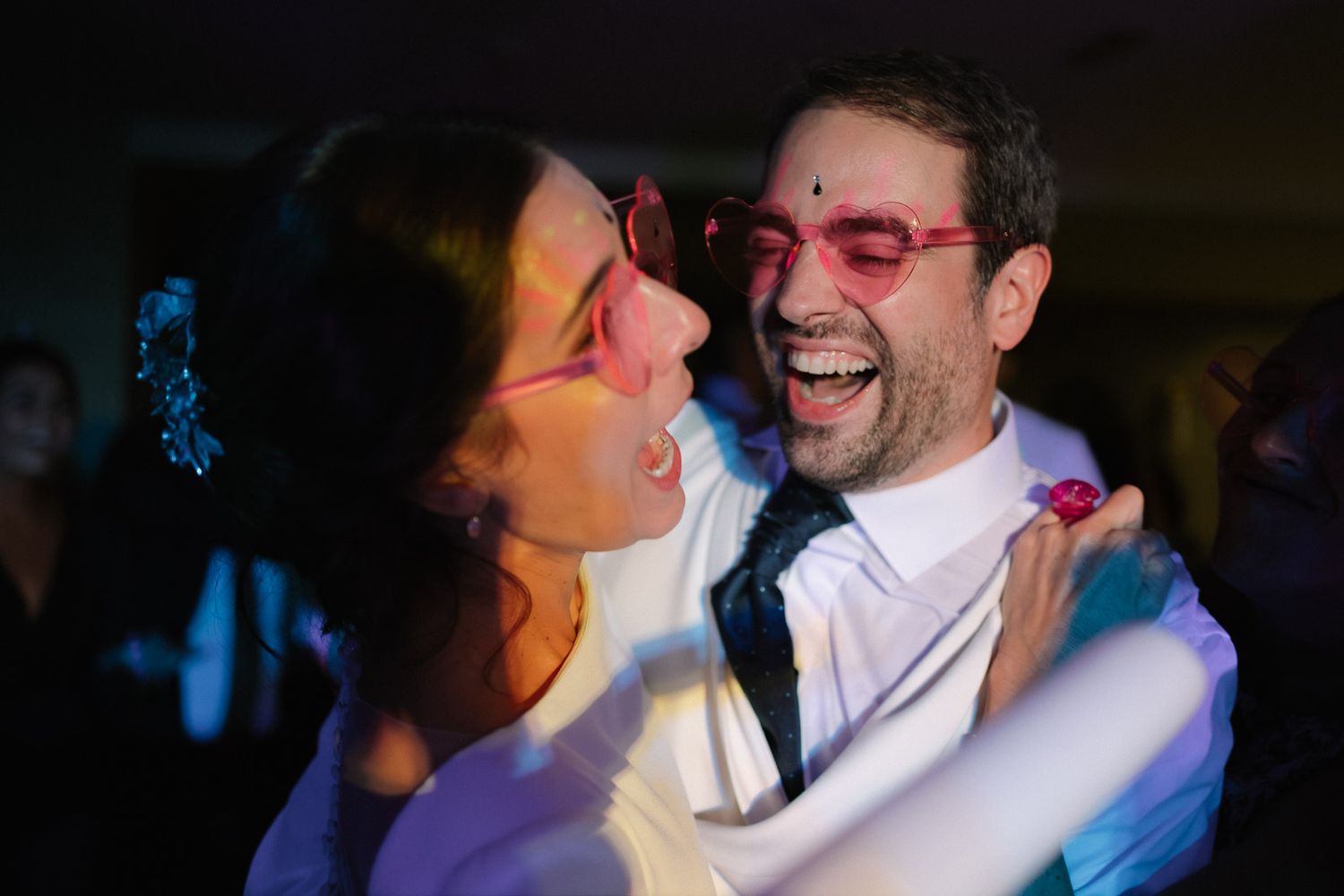 Joyful couple dancing and laughing together wearing pink sunglasses at a lively party celebration.