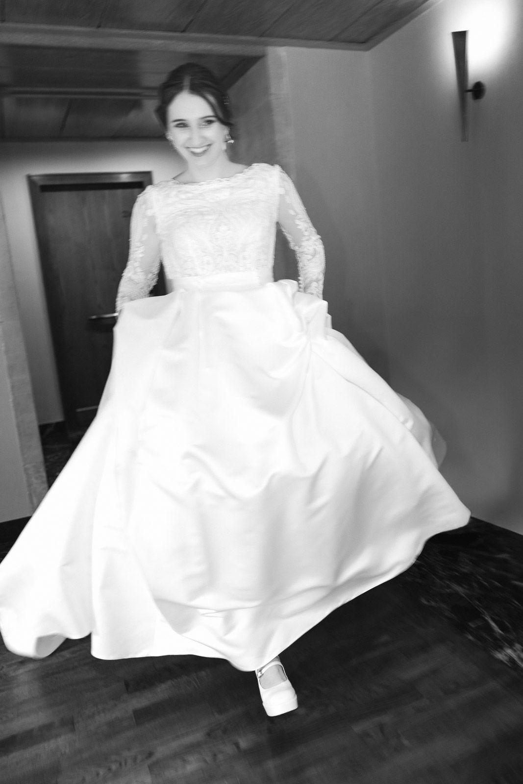 Black and white photo of smiling bride twirling in long-sleeve lace ball gown wedding dress.