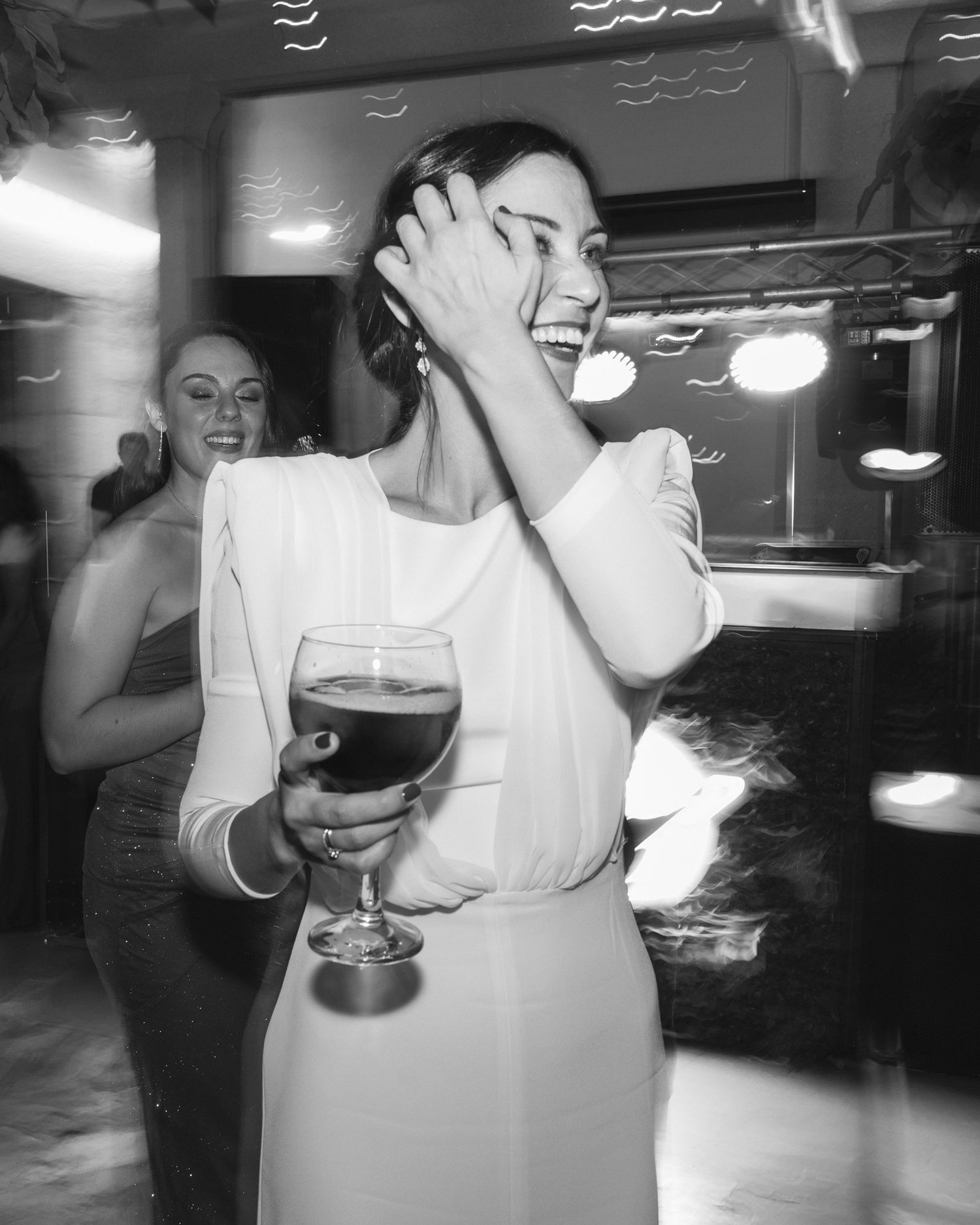 Vintage black and white photo showing a woman in a white dress laughing with a large wine glass at a party.