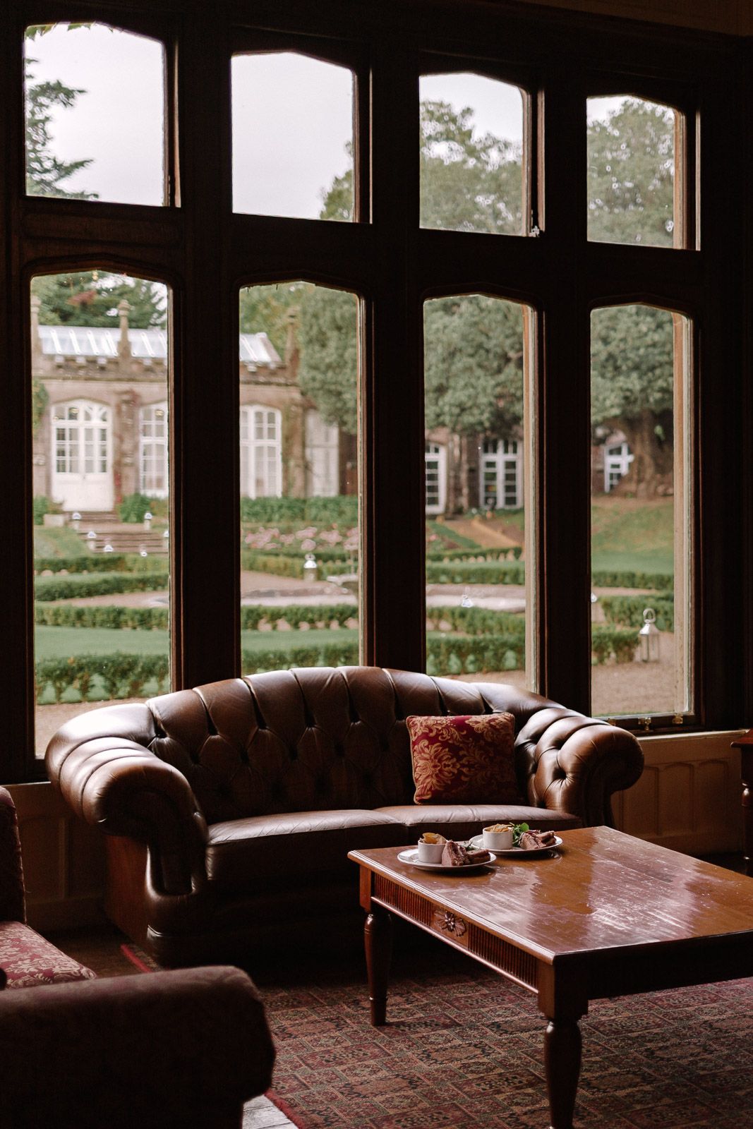 Luxurious leather Chesterfield sofa in a classic manor house interior overlooking formal garden grounds.