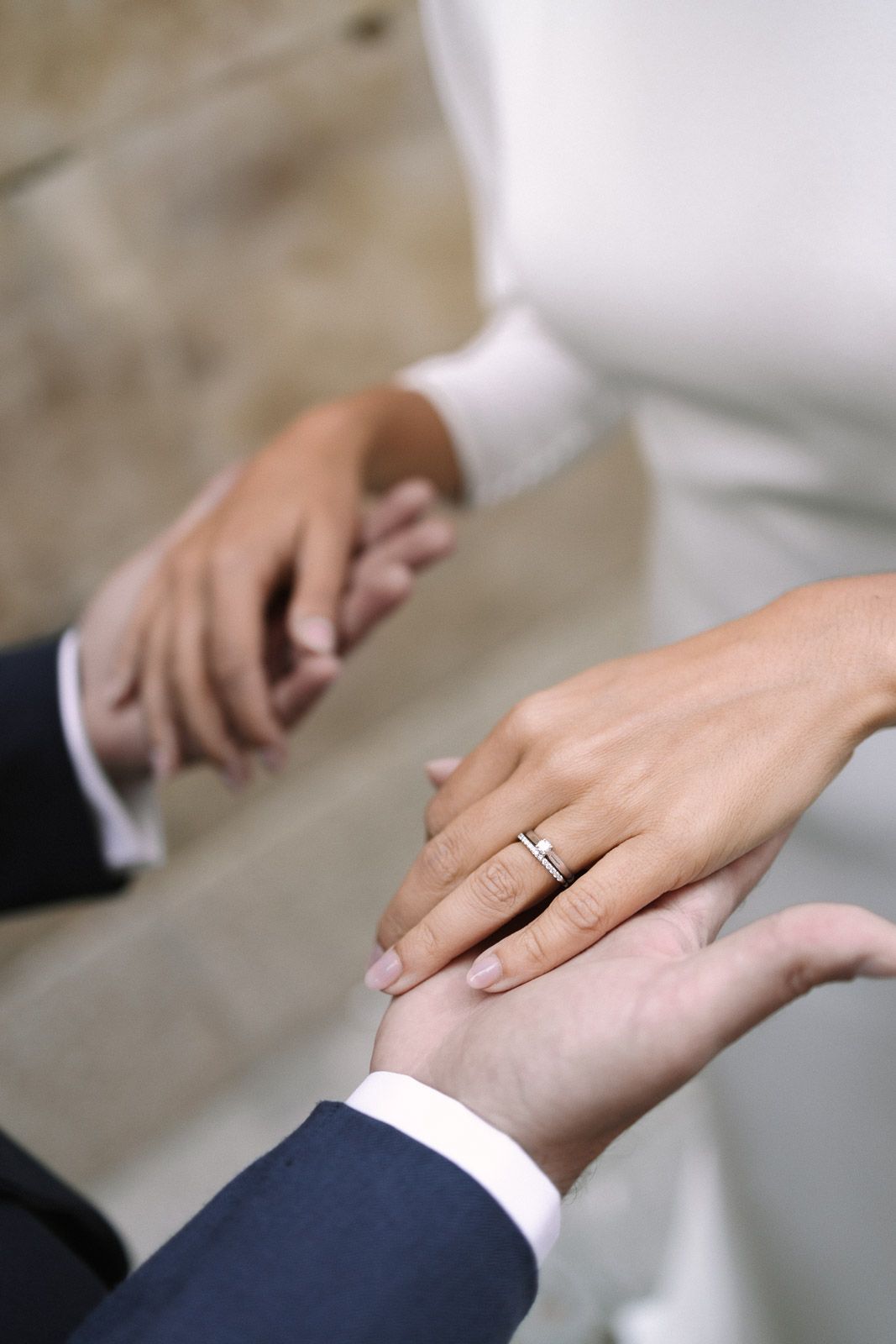 Bride and groom holding hands showing diamond engagement ring during wedding ceremony.