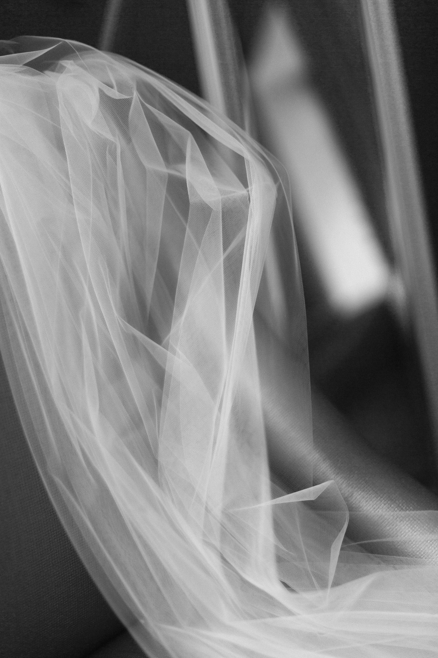Close-up black and white photograph of flowing delicate wedding veil tulle fabric with soft folds and texture.