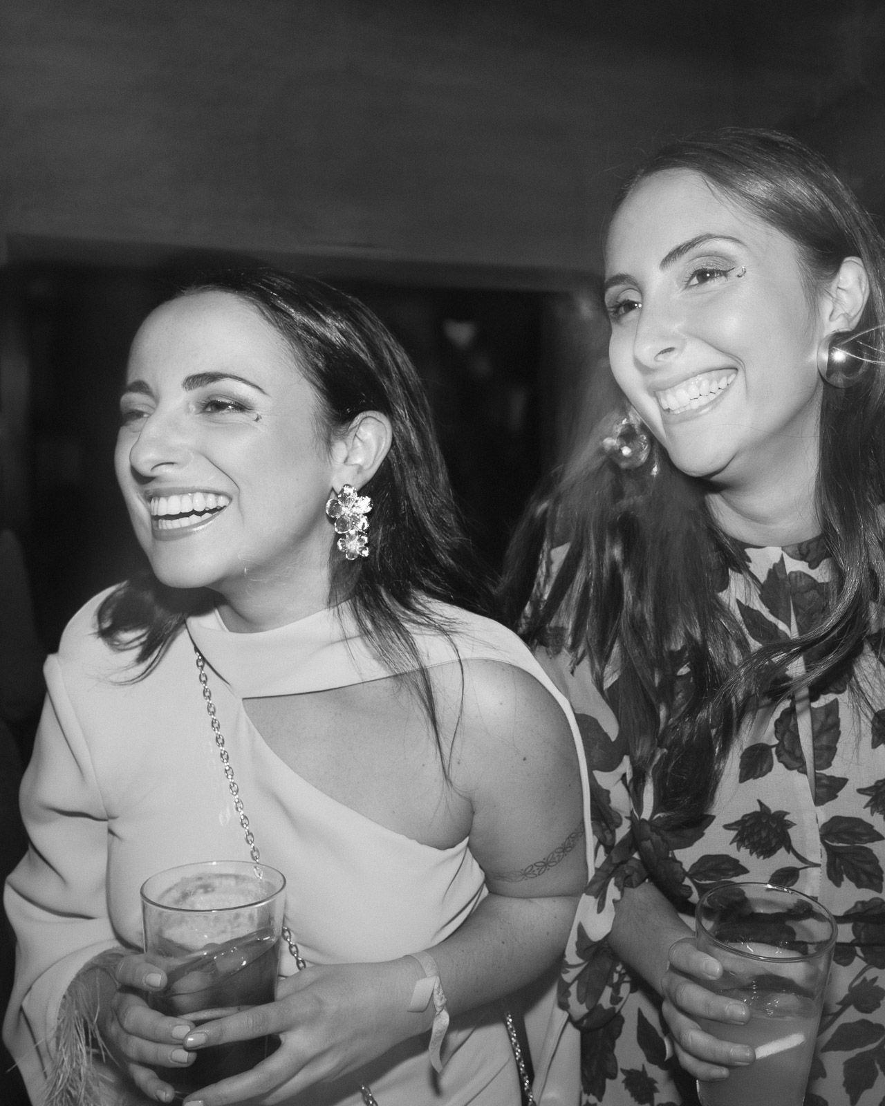 Two women laughing and holding drinks at a party in black and white photo.