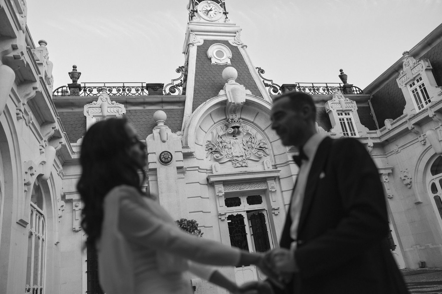 Black and white photo of bride and groom holding hands before ornate historic building.