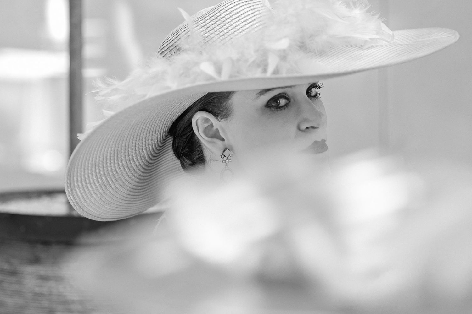 Elegant woman in a wide-brim white hat with feathers, captured in black and white photography.