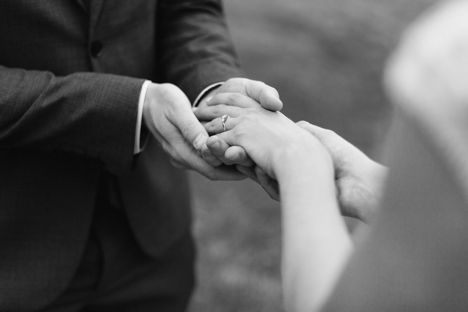 Black and white wedding photo of groom placing a ring on bride's finger during ceremony.