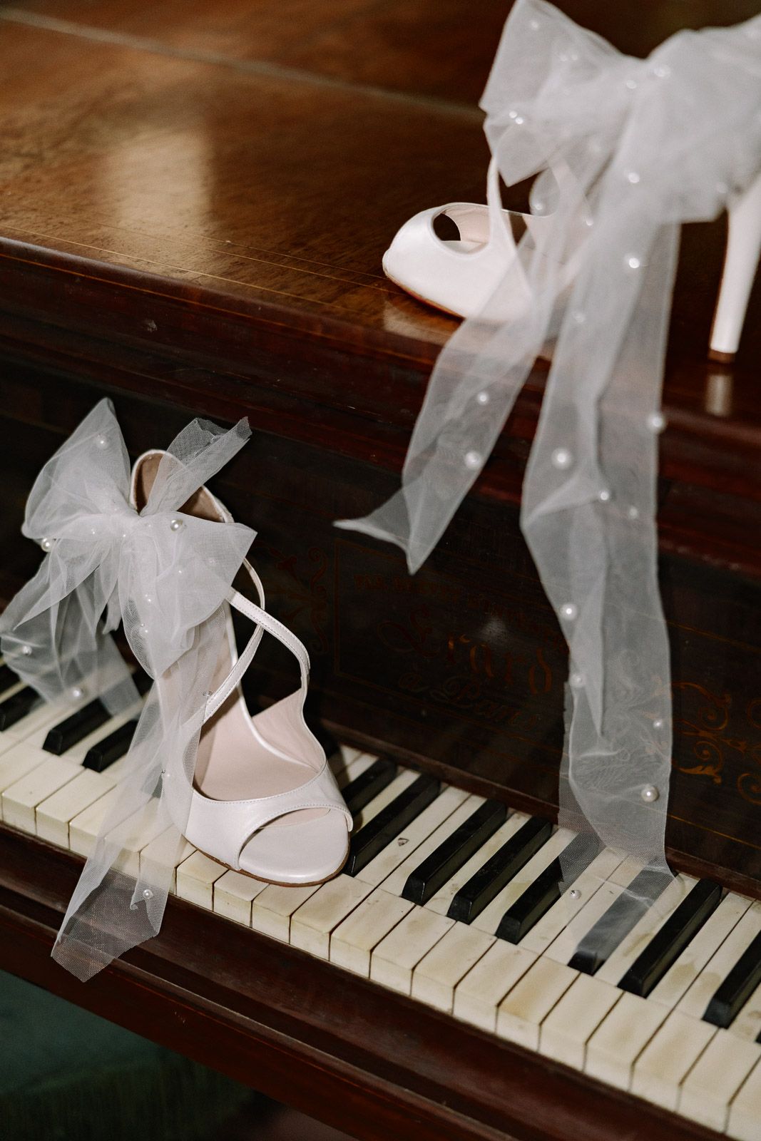 Elegant white bridal heels with tulle ribbon bows displayed on vintage piano keys for a wedding.