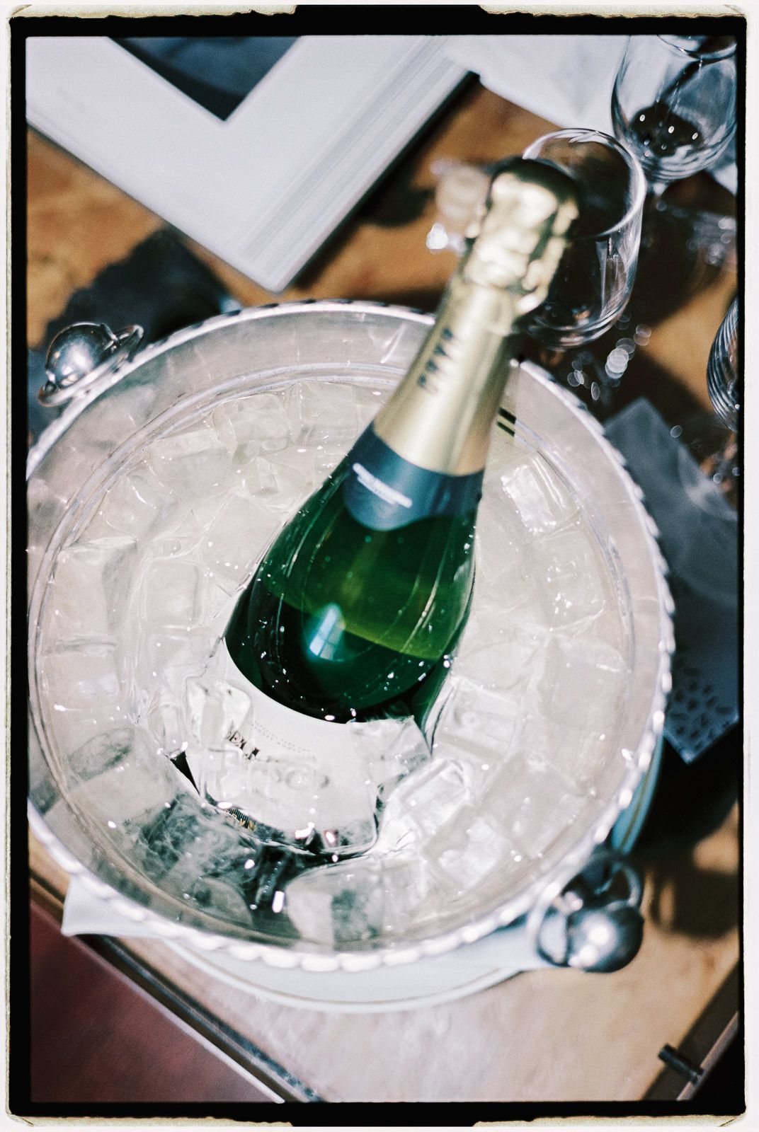 A chilled champagne bottle in an ice bucket with glasses on a wooden table.