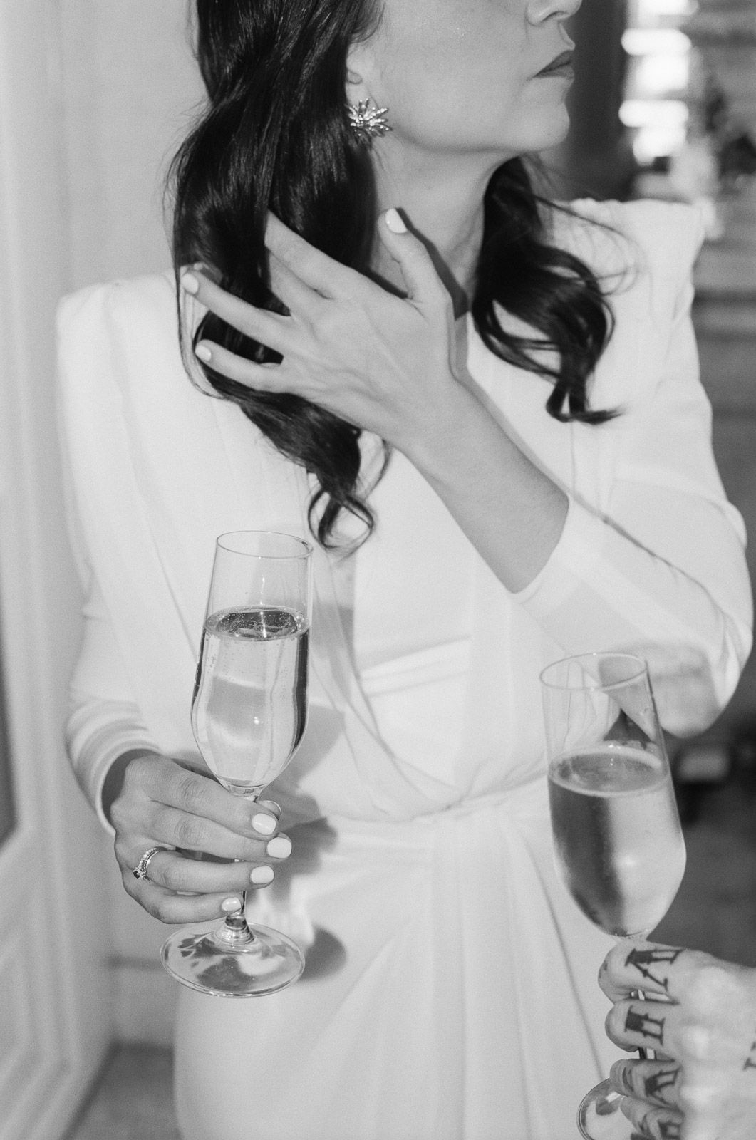 Elegant bride in white gown holding champagne flute, black and white wedding reception photo.