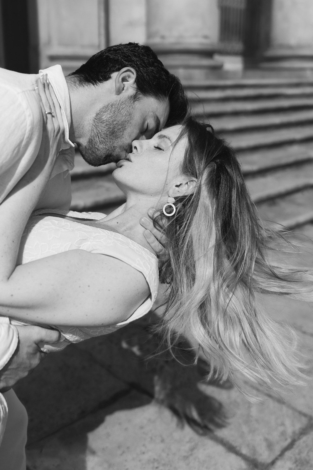 Black and white photo of a romantic couple sharing a passionate kiss near stone steps.