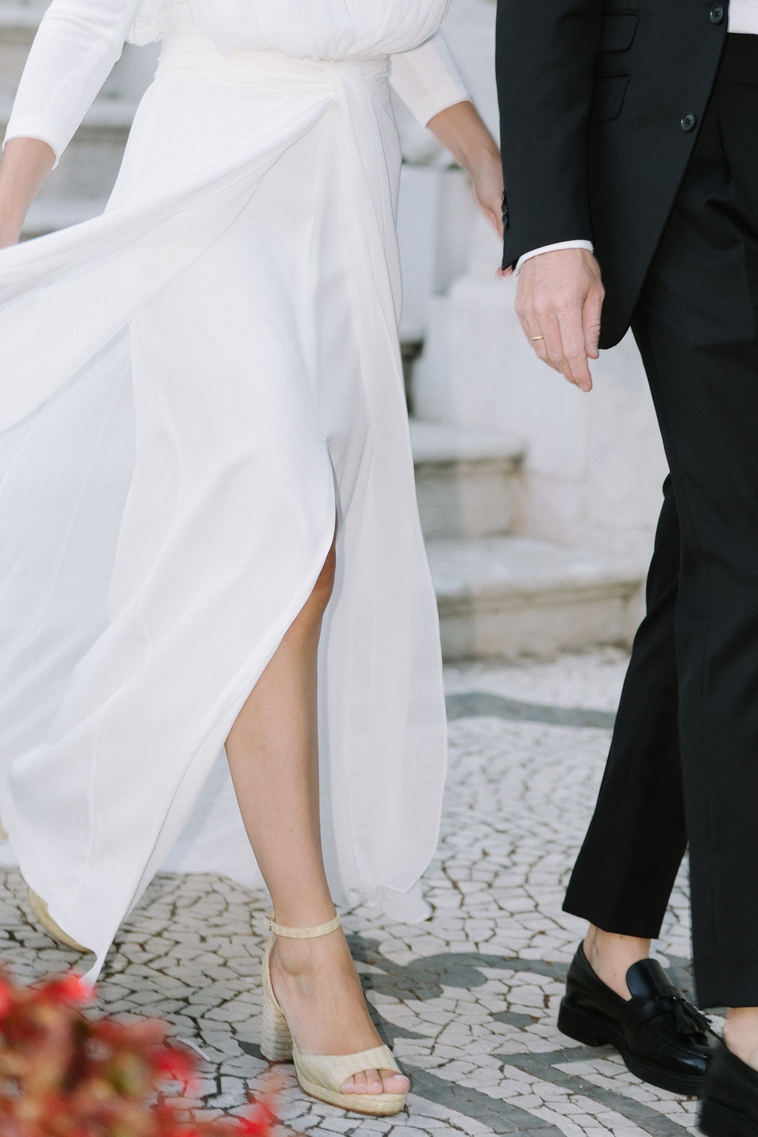 Close-up view of elegant flat wedding sandals in white with embellished details on a cobblestone path.