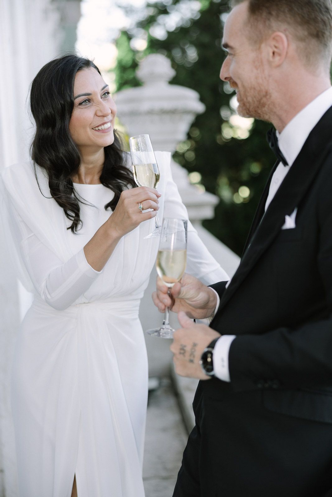 Elegant bride and groom toasting with champagne glasses at a classic white columned venue.