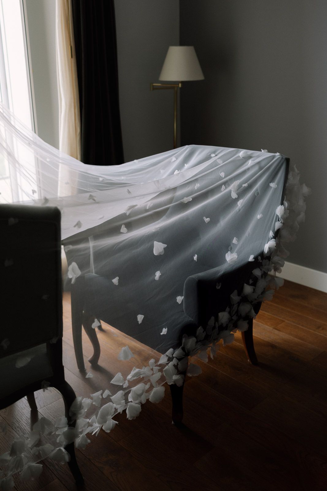 A delicate white wedding veil with floral appliques draped over an elegant chair in a softly lit room.