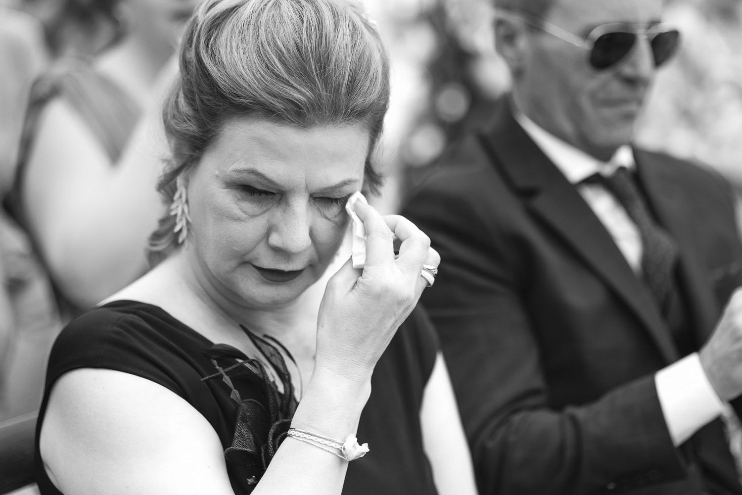 Emotional woman wiping tears at outdoor wedding ceremony in black and white photo.